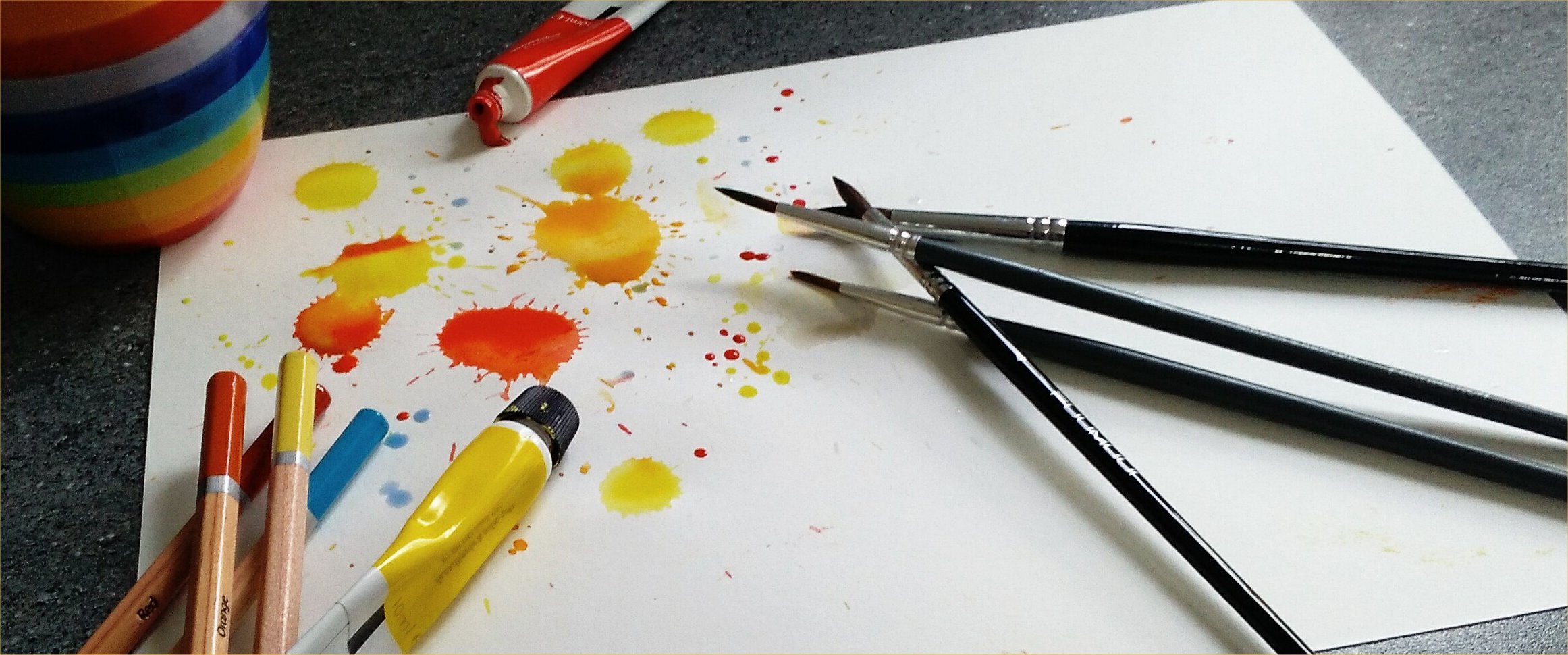 Splashed paint with brushes and pencils layed on paper